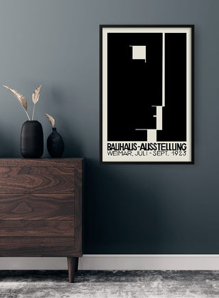 Framed Bauhaus Weimar 1923 poster with geometric design, displayed on a dark wall above a wooden dresser.