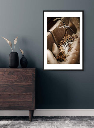 Framed Cartier poster featuring a lounging leopard on a beige tufted sofa, displayed above a modern dresser.