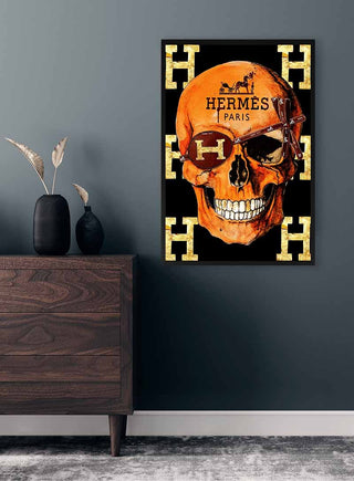 Hermes Skull Plakat featuring an orange skull with Hermes Paris text and gold H motifs, displayed on a dark wall.