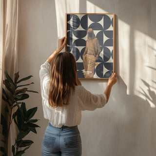 Woman hanging framed 1978 Annie Collection by Frank Moth art print on a sunlit wall above a houseplant.