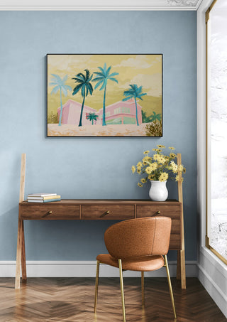 Framed print of The Pink House - Goed Blauw hanging above a wooden desk in a modern, light blue room.